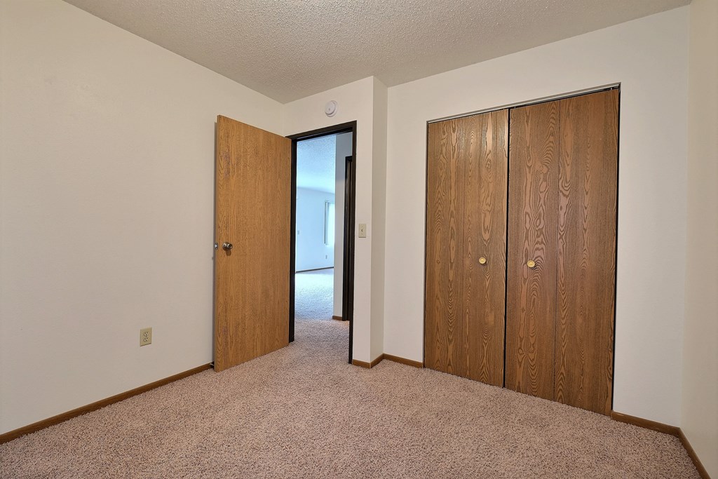 a bedroom with two closet doors and a door to a hallway. Fargo, ND Pacific South Apartments