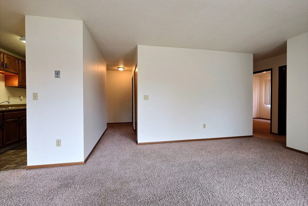 an empty living room with white walls and carpet. Fargo, ND Pacific South Apartments