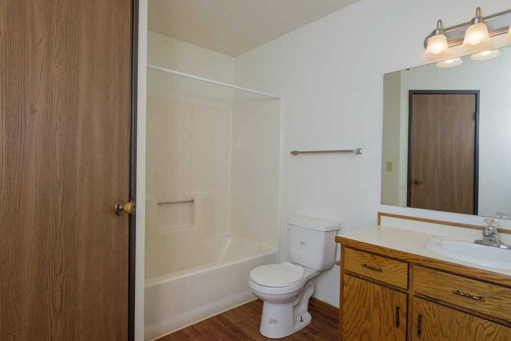 a bathroom with a toilet and a sink and a shower. Fargo, ND Park Circle Apartments.