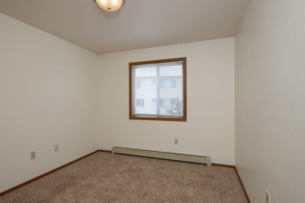 the living room of an empty home with carpet and a window. Fargo, ND Park Circle Apartments.
