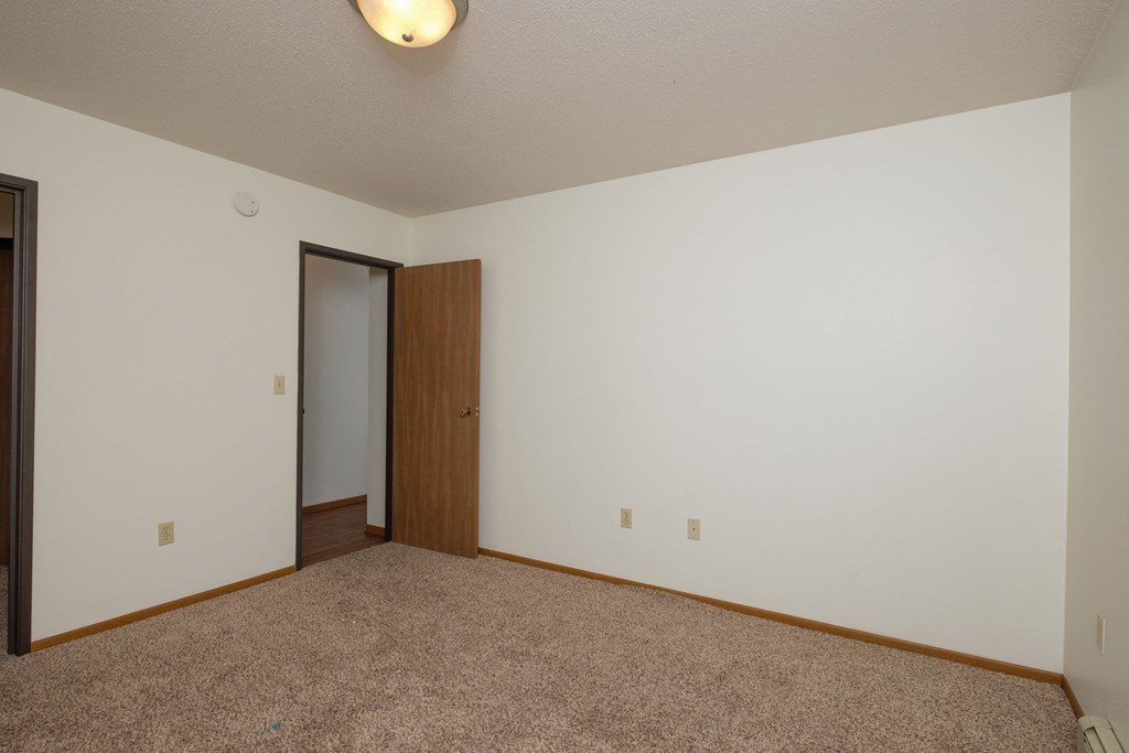 a bedroom with carpet and a door to a closet. Fargo, ND Park Circle Apartments.