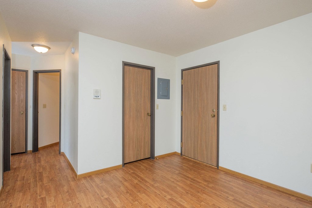 the living room of an empty apartment with wood flooring and three doors. Fargo, ND Park Circle Apartments.