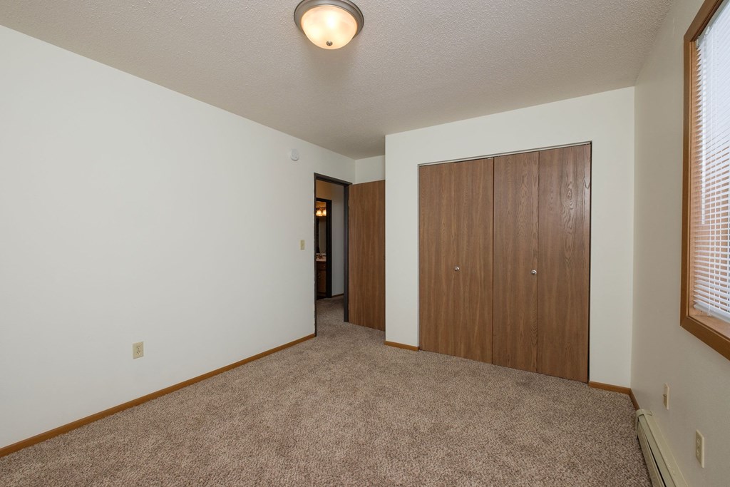 A bedroom with carpet and a closet. Fargo, ND Park Circle Apartments.
