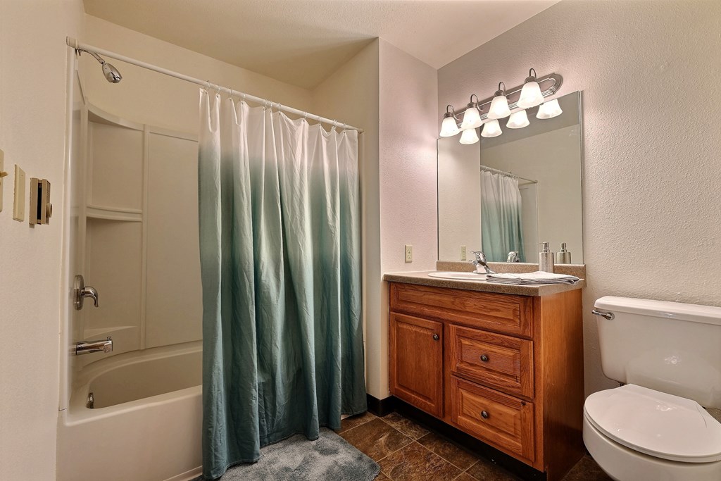a bathroom with a shower toilet and sink and a mirror. Fargo, ND Prairiewood Courts Apartments