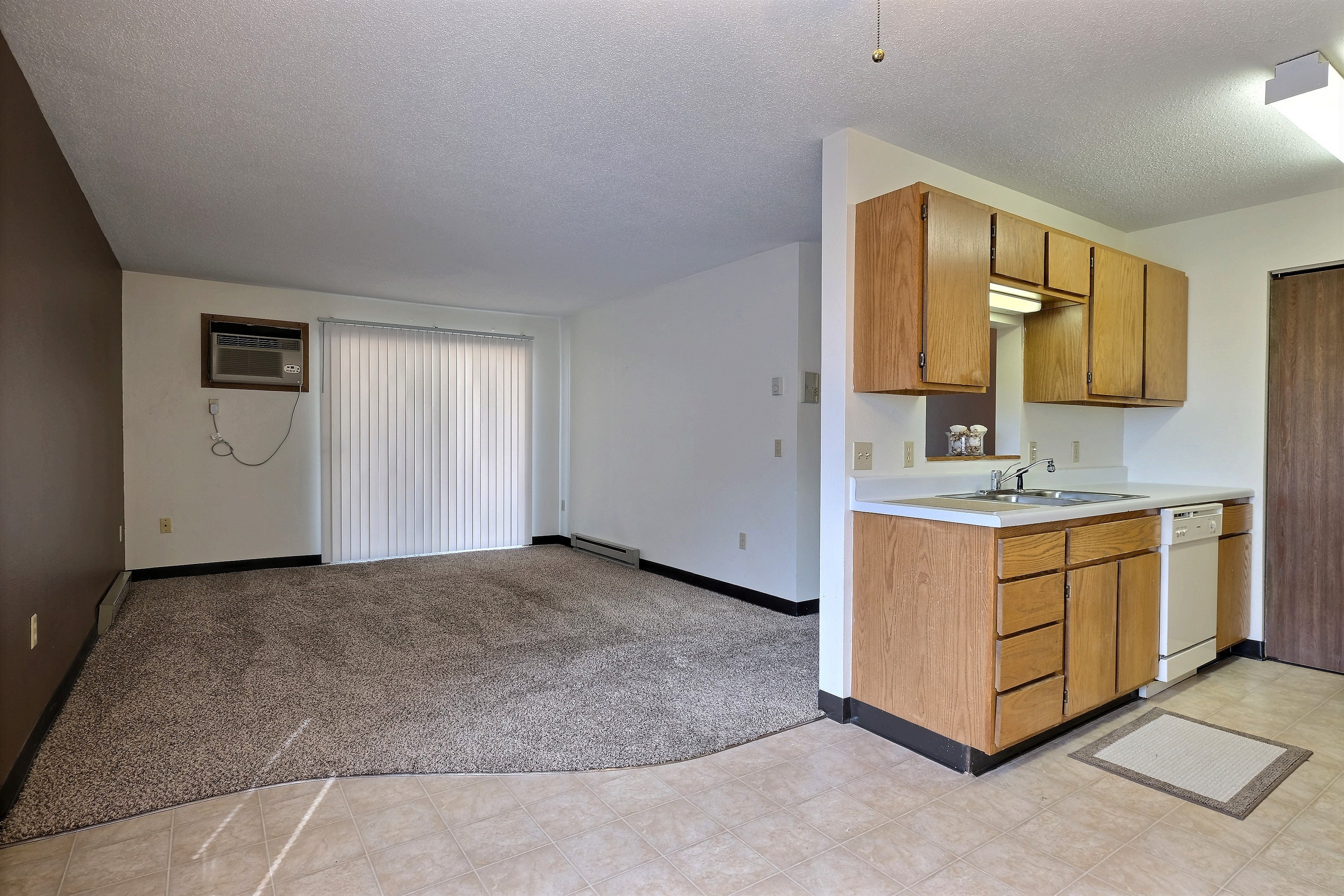 A living room with a glass sliding door with a kitchen. Fargo, ND Prairiewood Meadows
