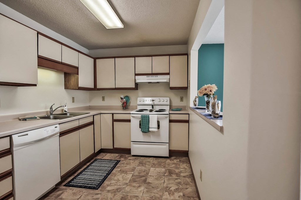 Grand Forks Primrose Apartments. A kitchen with a white stove top oven next to a sink and a dishwasher