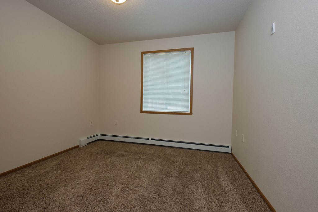 an empty bedroom with carpet and a window. Fargo, ND North Sky Apartments