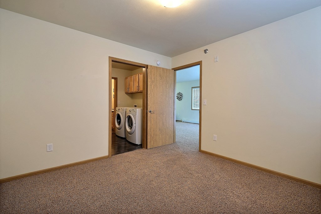 a bedroom with a door to a laundry room with a washer and dryer. Moorhead, MN Sandy Creek Apartments