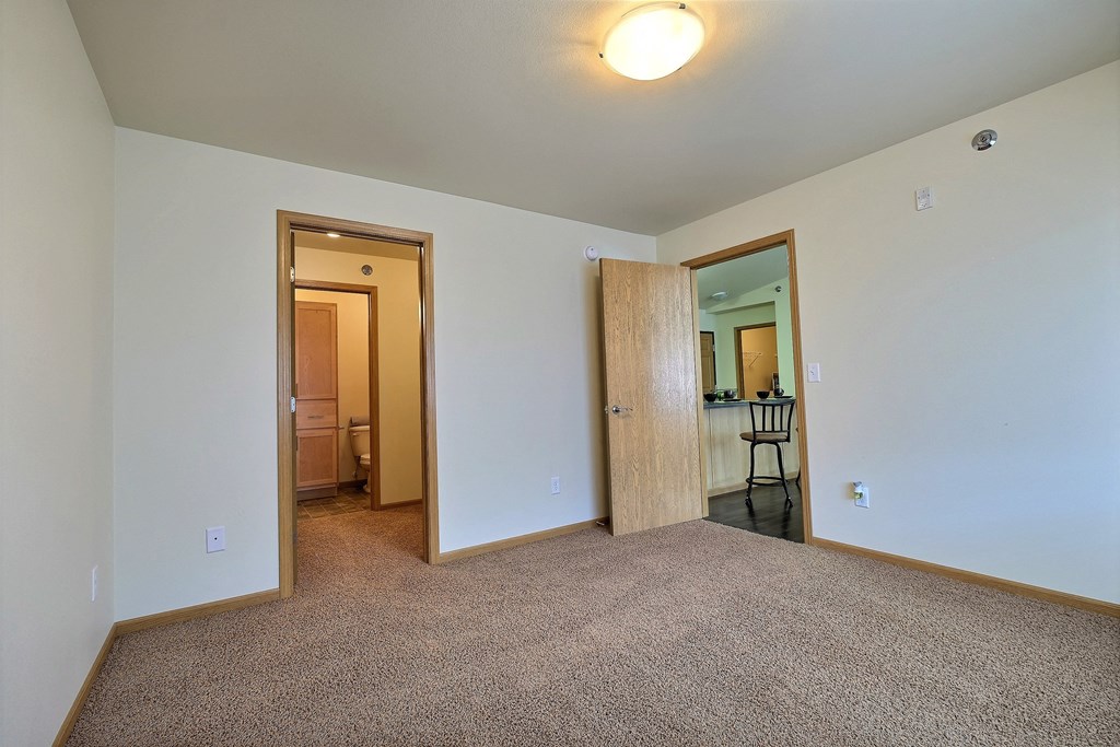 a bedroom with carpet and a door to a bathroom. Moorhead, MN Sandy Creek Apartments