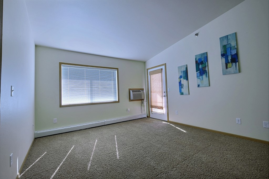 a living room with white walls, a window, and a door. Moorhead, MN Sandy Creek Apartments