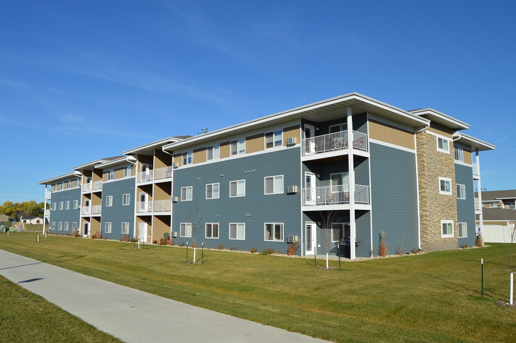 an exterior view of an apartment building with a green lawn. Moorhead, MN Sandy Creek Apartments