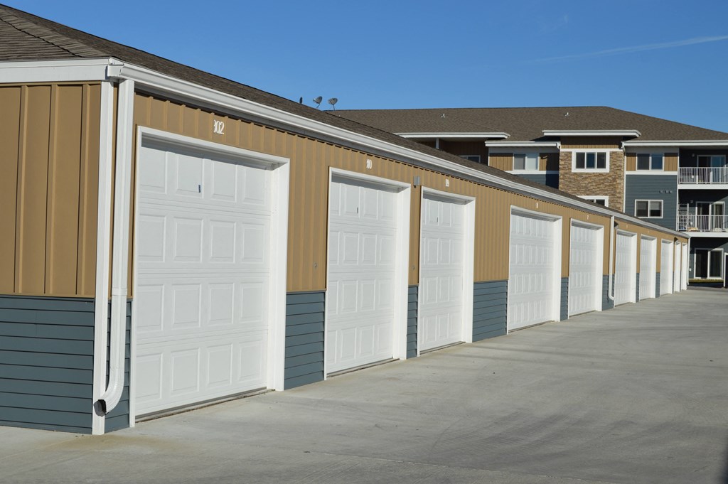 a row of garages with white doors in front of an apartment building. Moorhead, MN Sandy Creek Apartments