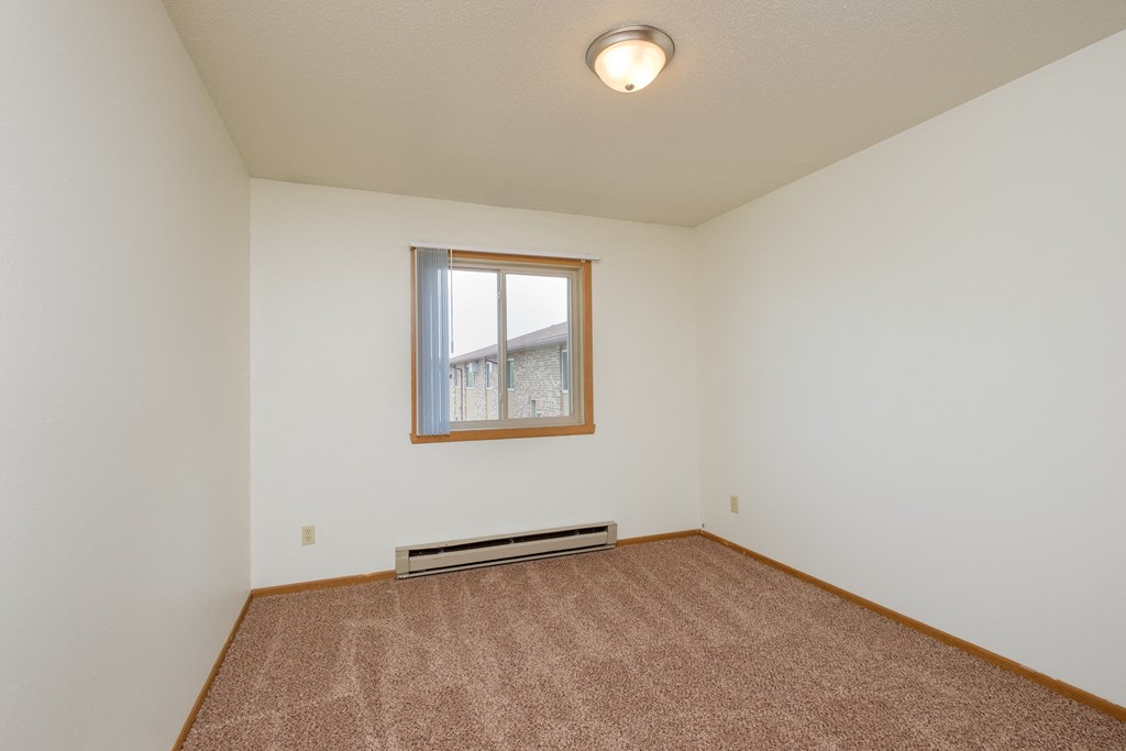 an empty living room with carpet and a window. Fargo, ND Sargent Apartments