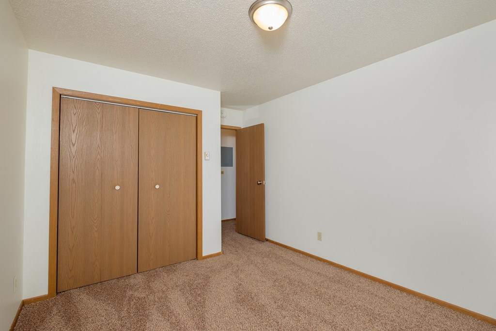 a spacious living room with carpet and a door to a bedroom. Fargo, ND Sargent Apartments