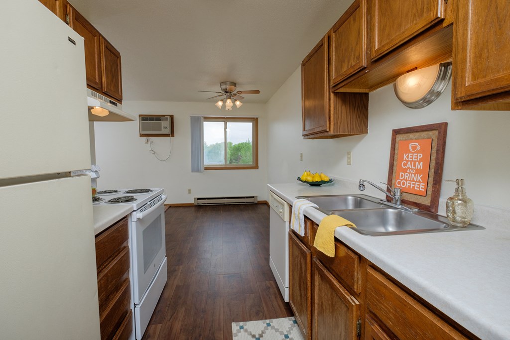 a kitchen with wooden cabinets and white appliances and a sink. Fargo, ND Sargent Apartments