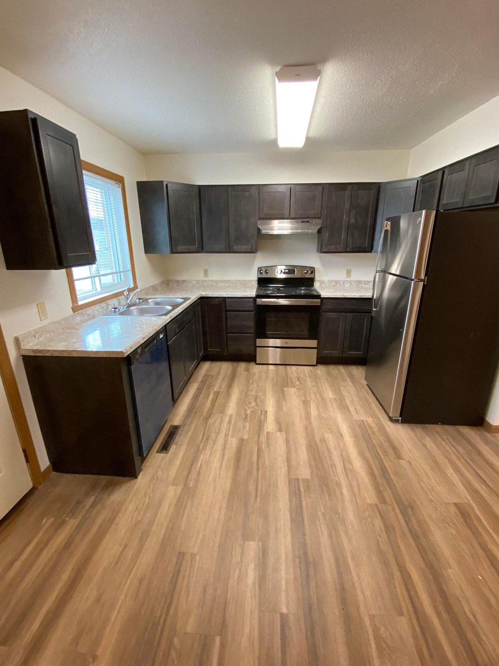 an empty kitchen with wooden floors and black cabinets. Fargo, ND Sheyenne Terrace