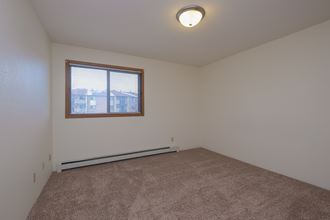 a bedroom with a window and a carpeted floor. Fargo, ND South Pointe Apartments
