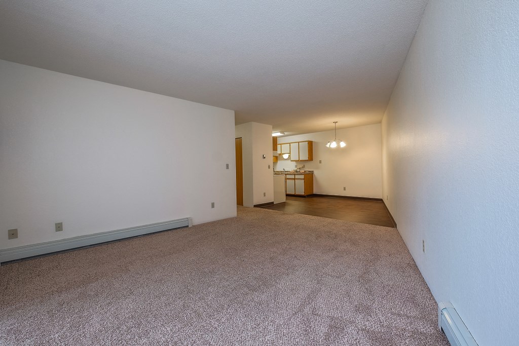 a living room with a kitchen and dining room in the background. Fargo, ND South Pointe Apartments