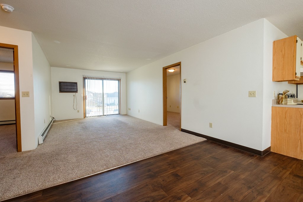 a living room with a glass sliding door and bedroom doors on the left and right. Fargo, ND South Pointe Apartments