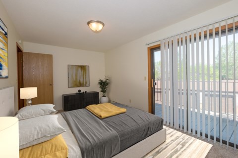 a bedroom with a bed and glass sliding door to a patio. Fargo, ND South Pointe Apartments