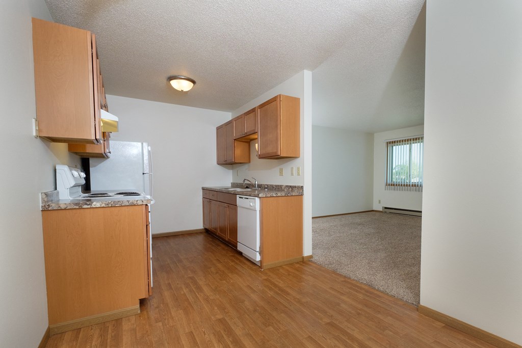a kitchen with white appliances and a living room in the background.Fargo, ND Southwind Apartments