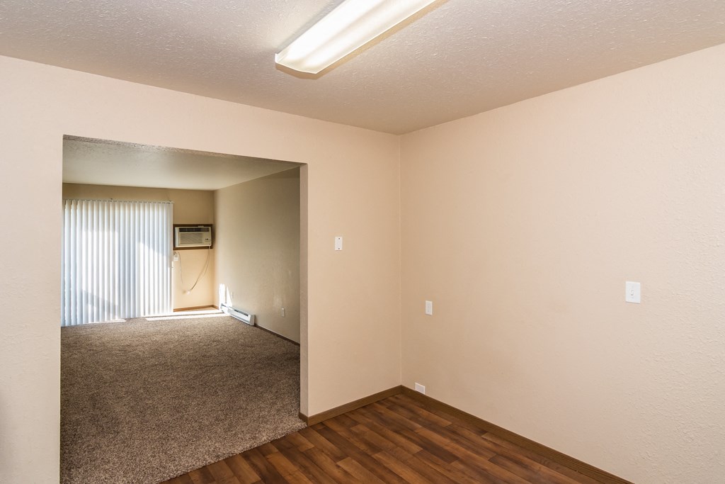 an empty living room with wood flooring and a door to a hallway. Grand Forks, ND Stanford Court Apartments