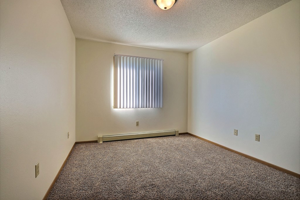 a spacious bedroom with carpet and a window. Fargo, ND Sterling Park Apartments