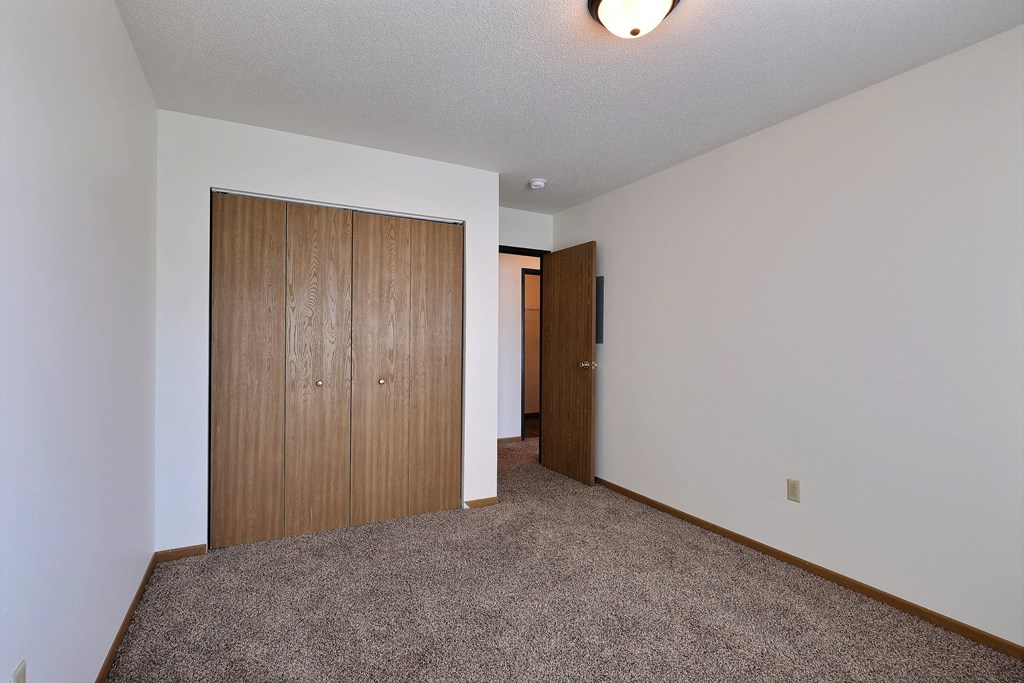 a bedroom with a closet and a door to a hallway. Fargo, ND Sterling Park Apartments