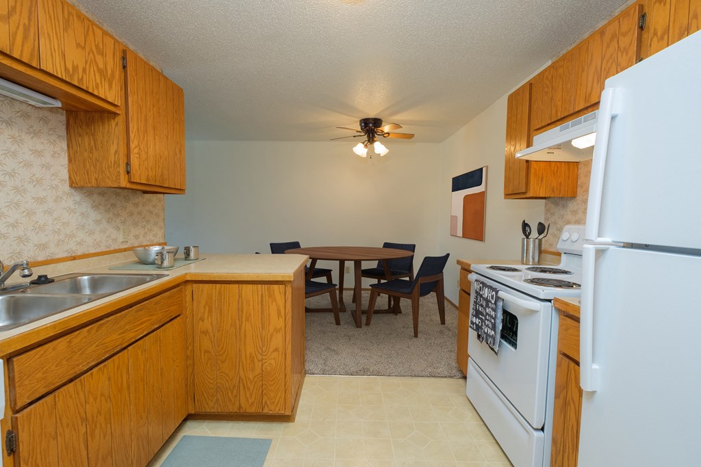 Fargo, ND Sugarplum Apartments. A kitchen and dining room. The dining room has a table with four chairs around it with a ceiling fan and light directly above it.