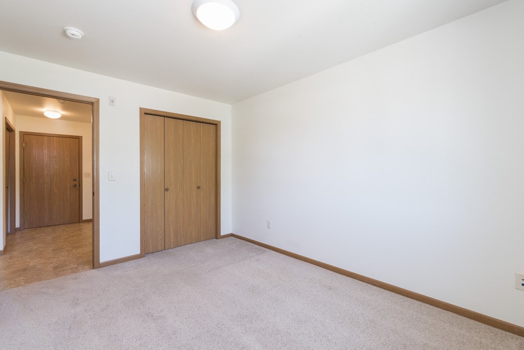 Empty living room with white walls and a door to a bedroom at Sunset Ridge Apartments in Bismarck, 58503 ND