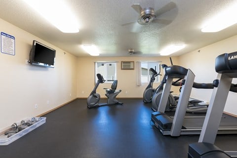 a gym with treadmills and other exercise equipment and a tv.Bismarck, ND Sunset Ridge Apartments