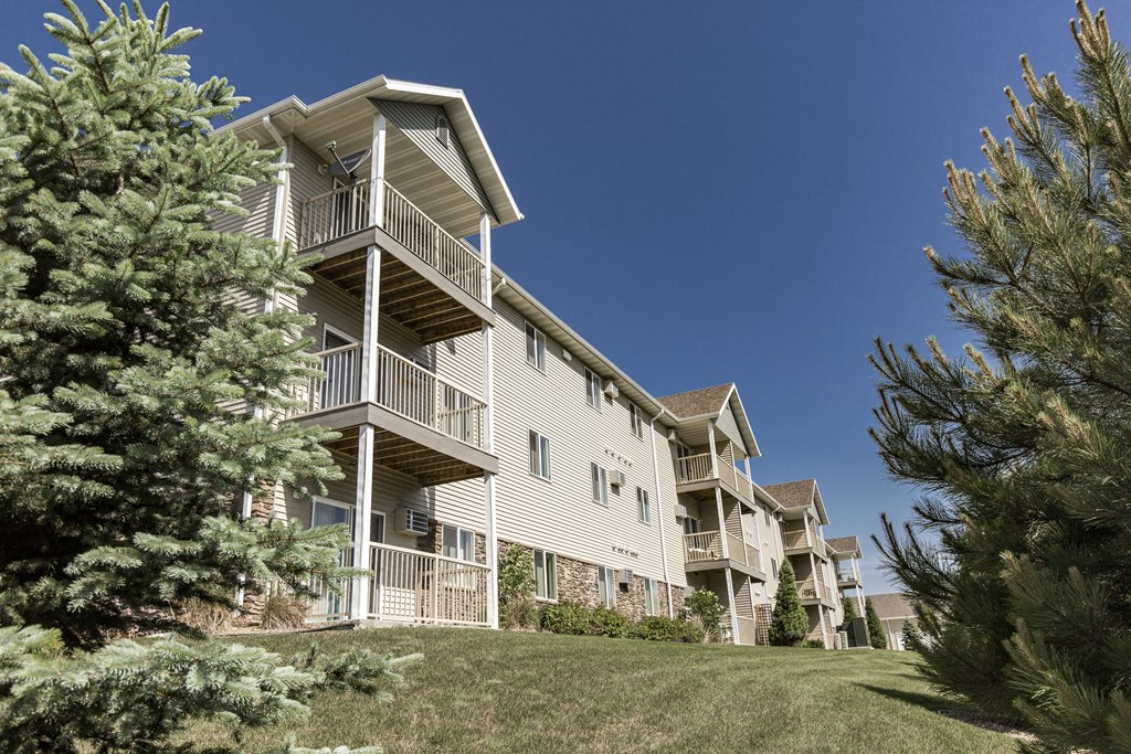 an apartment building with a lawn and trees in front of it. Bismarck, ND Sunset Ridge Apartments