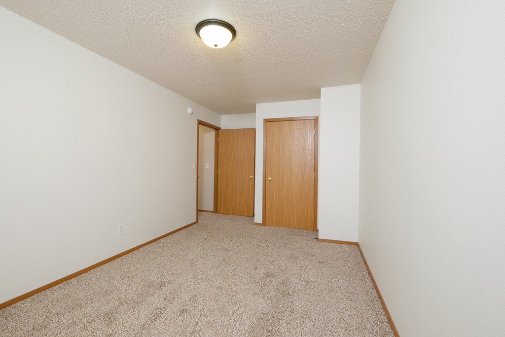 a spacious living room with carpet and a door to a bedroom. Fargo, ND Thunder Creek Apartments | KitchenFargo, ND Thunder Creek Apartments
