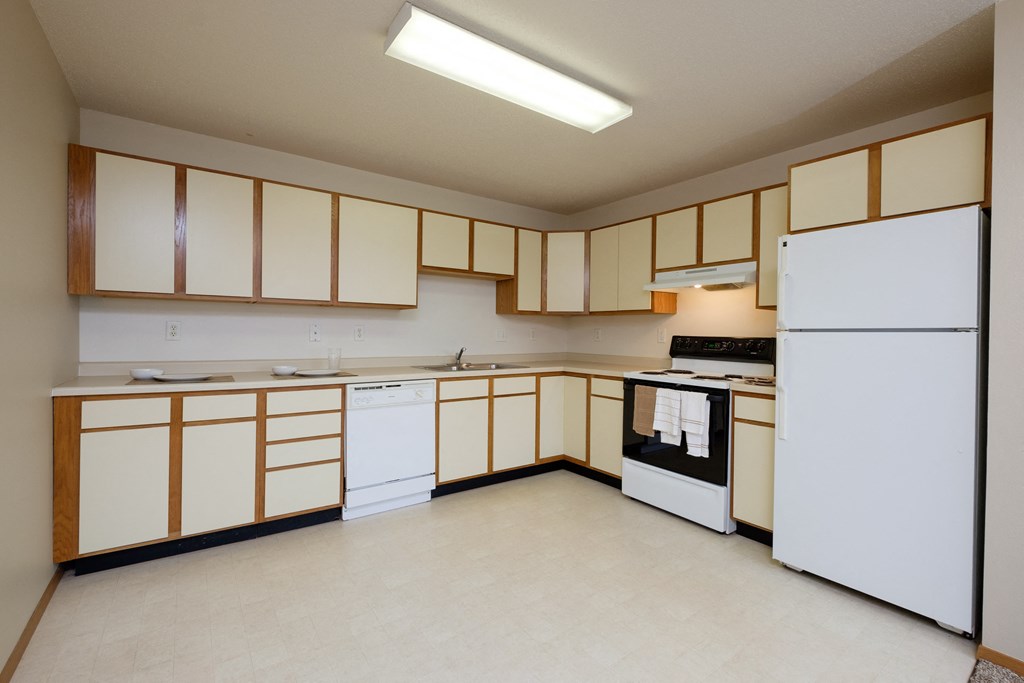 an empty kitchen with white appliances and wooden cabinets. Fargo, ND Thunder Creek Apartments