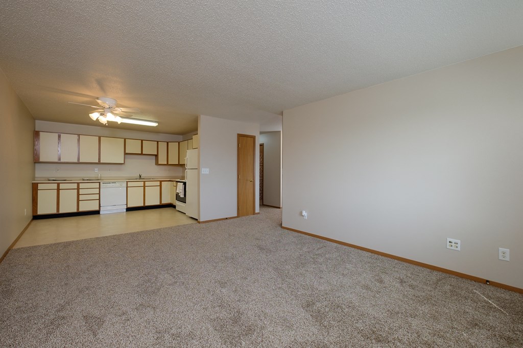 the living room and kitchen of an apartment with carpeting and a ceiling fan. Fargo, ND Thunder Creek Apartments