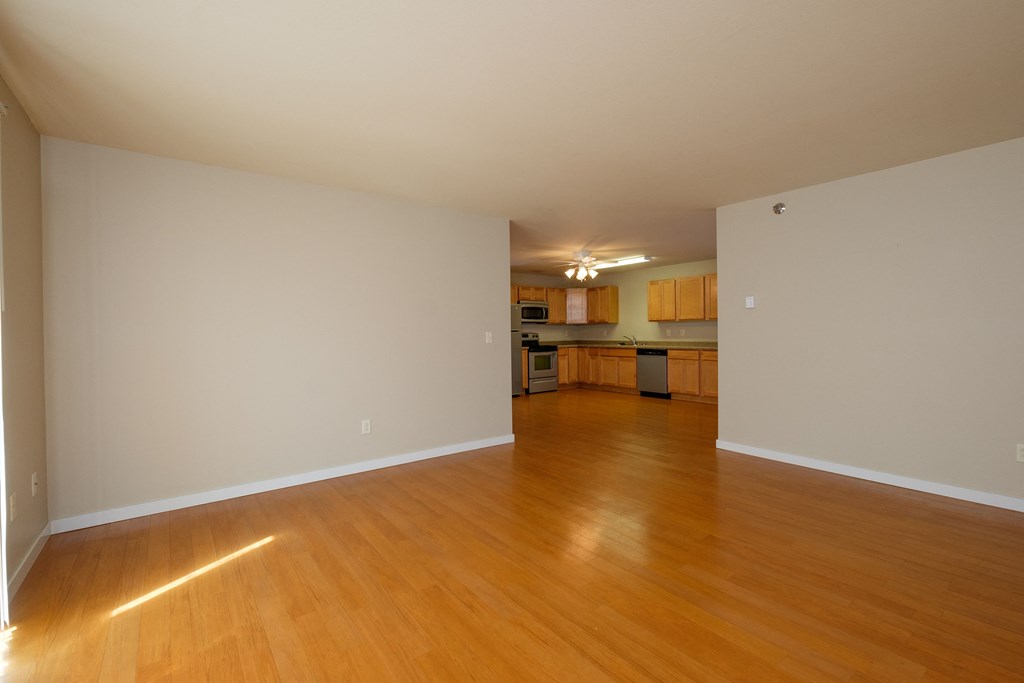 an empty living room with a hardwood floor and a kitchen in the background. Fargo, ND Thunder Creek Apartments