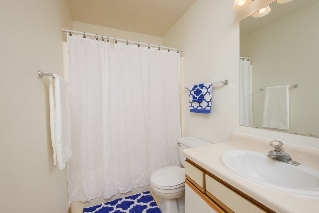 a bathroom with a white shower curtain and a sink and a toilet. Fargo, ND Twin Parks Apartments.
