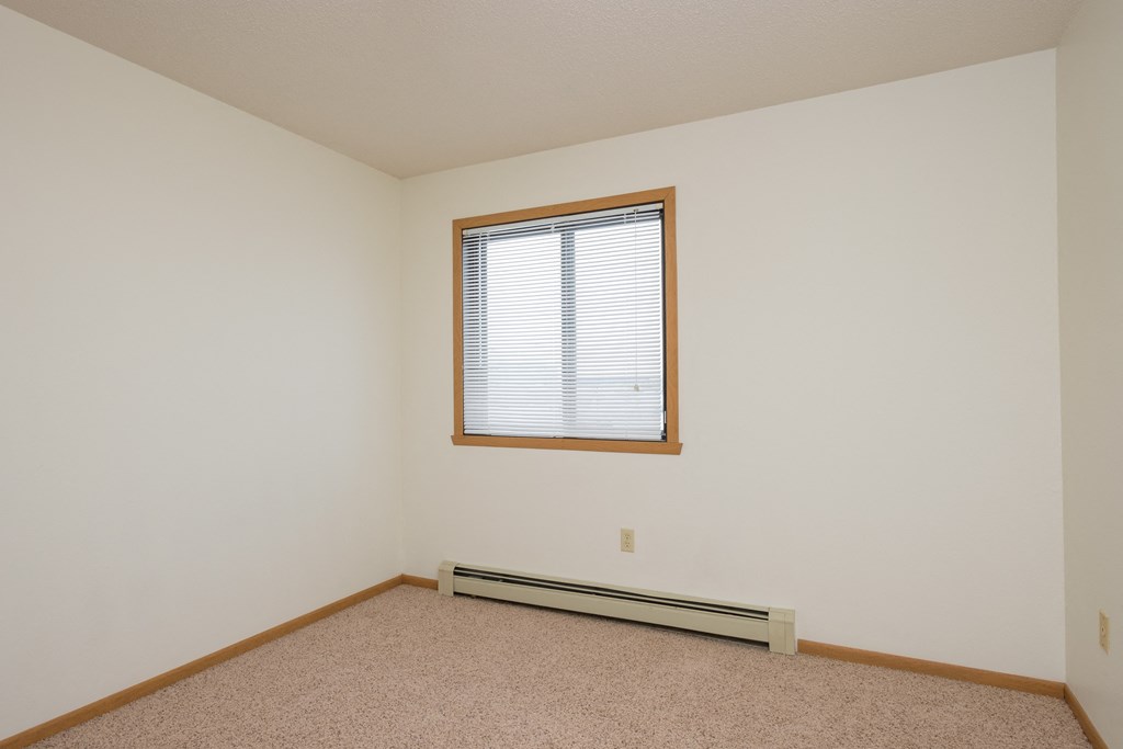 a bedroom with white walls and a window and a carpet. Fargo, ND Twin Parks Apartments.