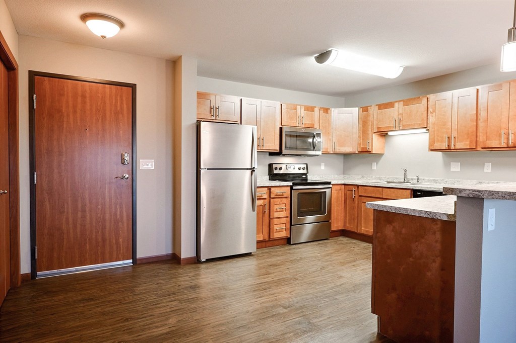a kitchen with wooden cabinets and a stainless steel refrigerator. Fargo, ND Urban Plains Apartments