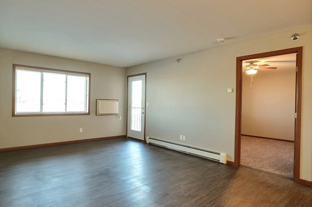 an empty living room with wood flooring and a window. Fargo, ND Urban Plains Apartments