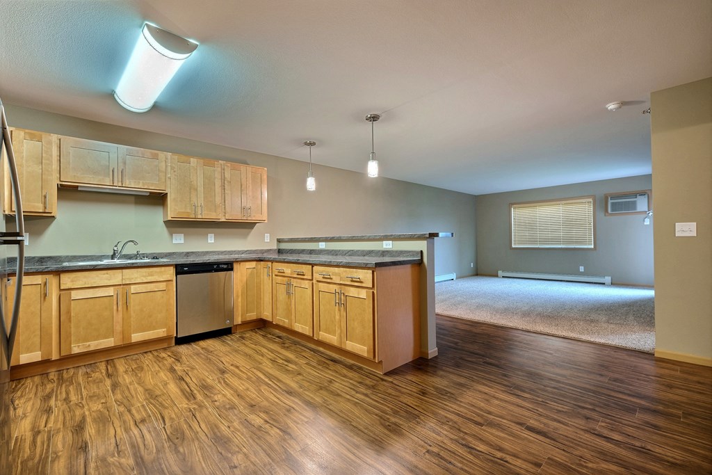an empty kitchen and living room with wood floors and wood cabinets. Fargo, ND Urban Plains Apartments
