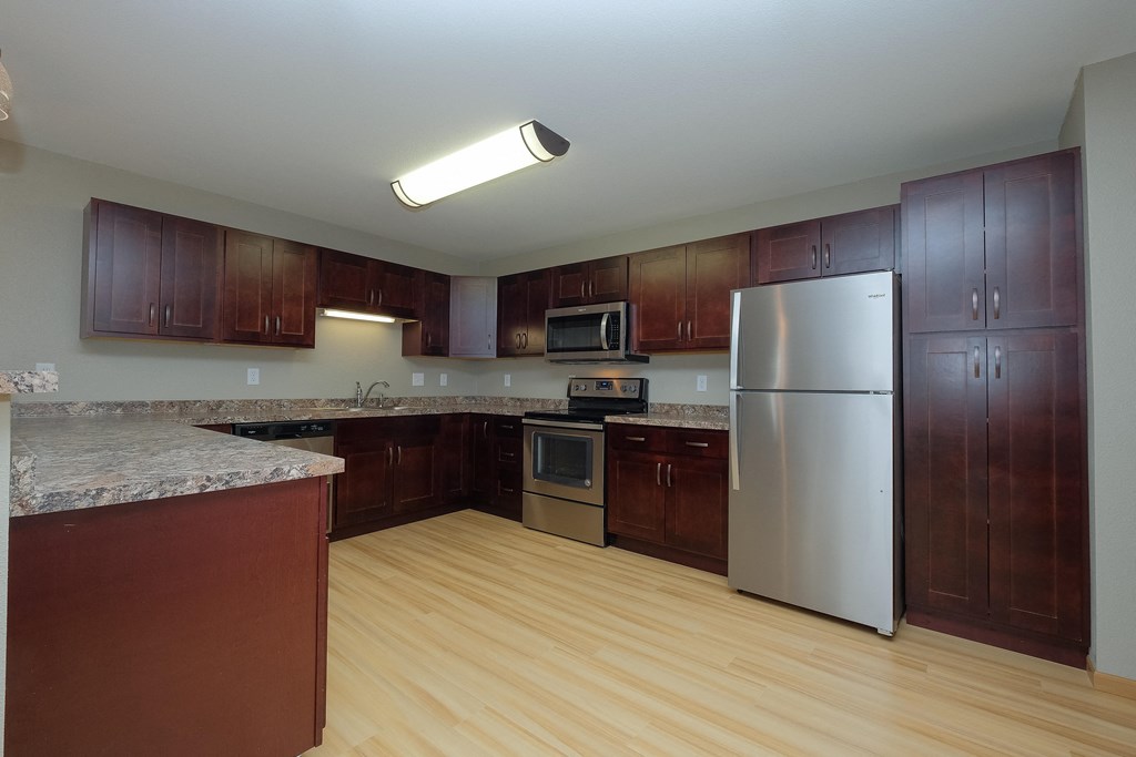 a kitchen with wooden cabinets and a stainless steel refrigerator. Fargo, ND Urban Plains Apartments