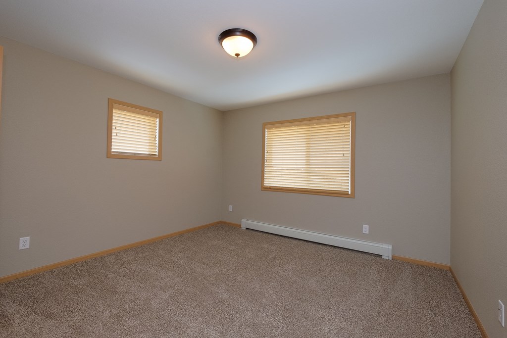 a bedroom with two windows and a carpet. Fargo, ND Urban Plains Apartments