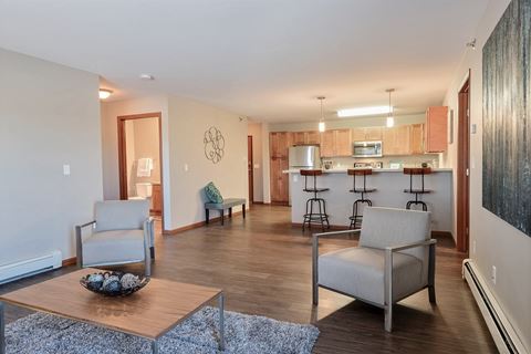 a living room with two chairs and a table in front of a kitchen. Fargo, ND Urban Plains Apartments