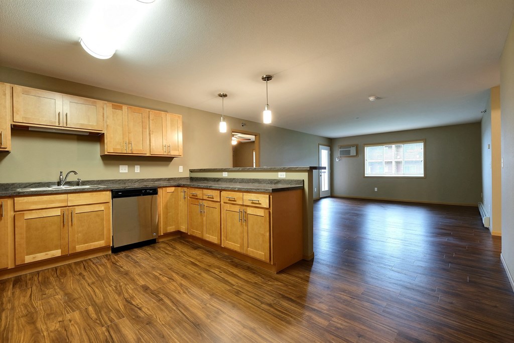 an empty kitchen and living room with wood floors and wood cabinets. Fargo, ND Urban Plains Apartments