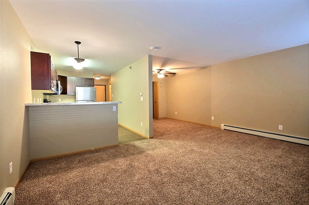 the living room and kitchen of an empty apartment with carpeting. Fargo, ND Urban Plains Apartments