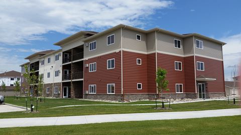 an exterior view of an apartment building with grass and a sidewalk. Fargo, ND Urban Plains Apartments