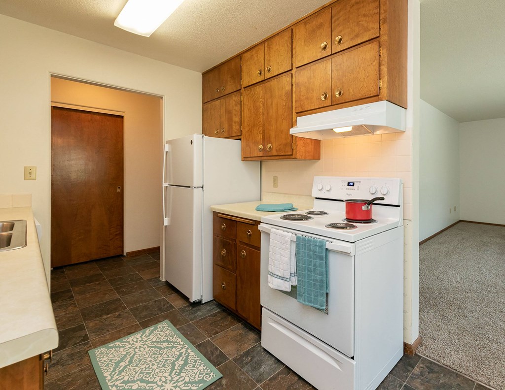a kitchen with white appliances and wooden cabinets and a white refrigerator. Fargo, ND Islander Apartments