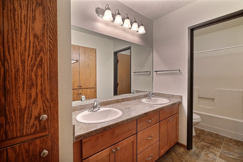 a bathroom with two sinks and a large mirror. Fargo, ND Village West Apartments