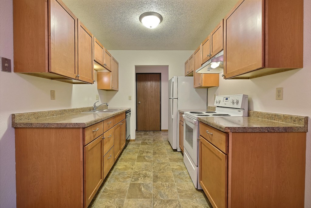 a kitchen with wooden cabinets and a white stove and refrigerator. Fargo, ND Village West Apartments